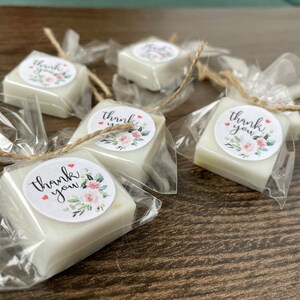 May include: Five small white square soaps wrapped in clear cellophane bags with a floral design and the text "thank you" on each soap.