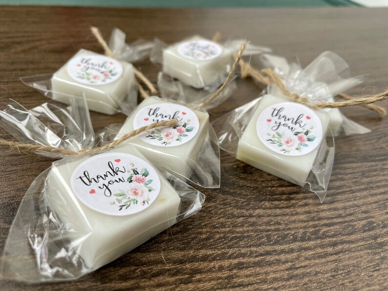 May include: Five small white square soaps wrapped in clear cellophane bags with a floral design and the text "thank you" on each soap.
