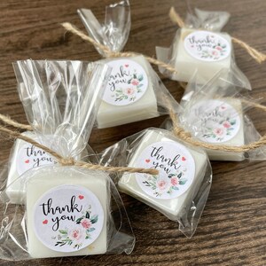 May include: Small white square soaps wrapped in clear cellophane bags with twine and a floral thank you sticker.