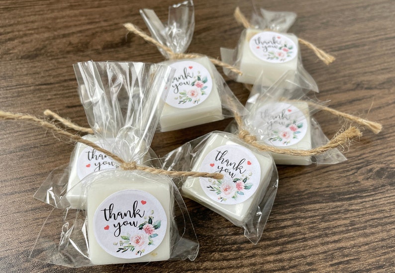 May include: Small white square soaps wrapped in clear cellophane bags with twine and a floral thank you sticker.