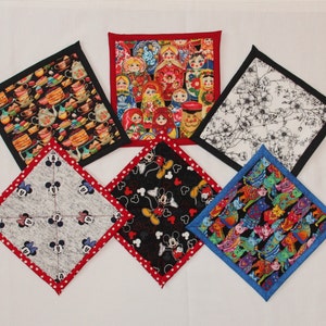 May include: Six different fabric squares with various patterns. The squares are all the same size and have a red, black, blue, or white border. The patterns include a teacup design, a Russian nesting doll design, a floral design, a Mickey Mouse design, a heart design, and a colorful cat design.