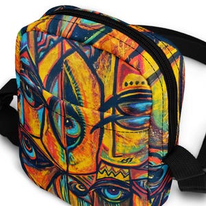 May include: A small, colorful crossbody bag with a vibrant abstract design. The bag features a repeating pattern of faces and geometric shapes in shades of yellow, orange, blue, and black. It has a black zipper and strap.