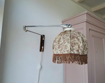 May include: A chrome wall-mounted lamp with a white and brown floral patterned lampshade with a brown fringe.