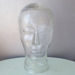 May include: A clear glass mannequin head with a textured surface. The head is on a white surface.