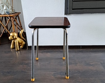 May include: A dark brown square stool with a chrome frame and yellow plastic feet.
