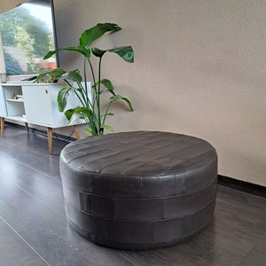 May include: A brown leather ottoman with a woven pattern. The ottoman is round and has a smooth surface.