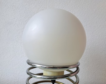 May include: A white globe lamp with a chrome spring base. The lamp is on a white background.