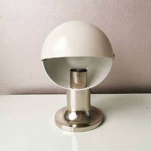 Op de afbeelding: Een witte en zilveren tafellamp met een ronde, halfronde kap. De lamp heeft een chromen voet en een witte kap.