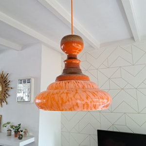 Op de afbeelding: Oranje en bruine keramische hanglamp met een witte marmeren kap. De lamp hangt aan een wit plafond.
