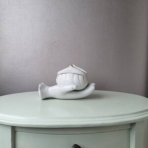 May include: White porcelain trinket box shaped like a hand holding a small, white, lidded bowl with gold trim.