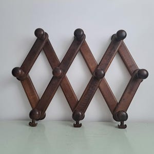 May include: A dark brown wooden coat rack in an accordion design. The rack has a series of diamond-shaped sections with rounded knobs at the intersections and hooks at the bottom. It is designed to expand and contract.