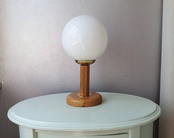 Puede incluir: Una lámpara de globo blanco con una base de madera y un acento de latón. La lámpara está sentada en una mesa azul claro con un cajón.