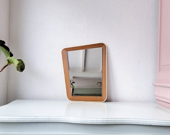 May include: A rectangular wooden framed mirror with a white border. The mirror is tilted at an angle and reflects a room with a white ceiling.