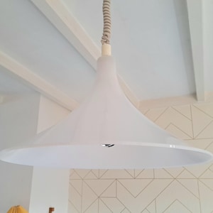 Op de afbeelding: Een witte, kegelvormige hanglamp hangt aan een wit plafond. De lamp heeft een eenvoudig, modern ontwerp.