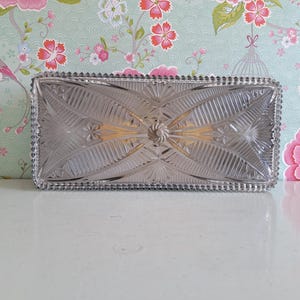 May include: A clear glass ceiling light fitting with a decorative, geometric pattern. The fitting has a beaded edge and a central, circular design.