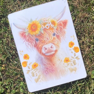 Puede incluir: Una vaca Highland con una corona de flores amarillas y blancas, pintada en estilo acuarela. La vaca mira directamente al espectador con una expresión dulce. El fondo es un blanco suave con algunas flores amarillas.