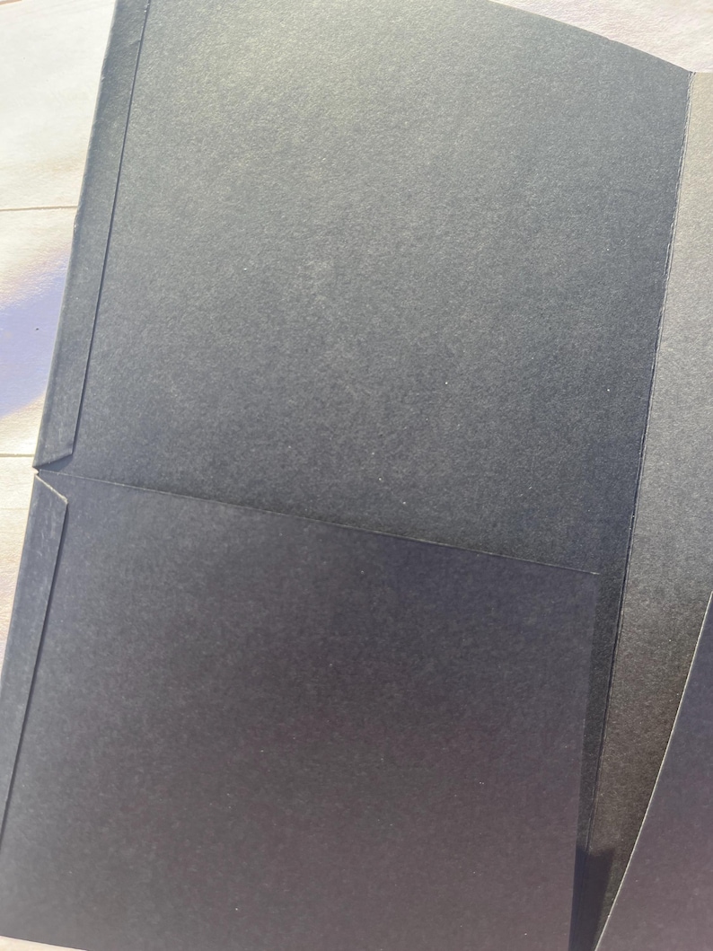 Peut inclure: Un porte-documents noir avec une surface textur&eacute;e. Le dossier a une poche &agrave; l'int&eacute;rieur et est ouvert, r&eacute;v&eacute;lant l'int&eacute;rieur. Le dossier est fait d'un mat&eacute;riau en papier &eacute;pais et durable.