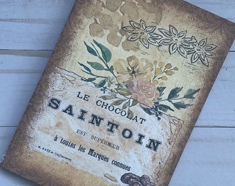 May include: Vintage style packaging for Le Chocolat Saint Oin, a chocolate brand. The packaging features a floral design with a brown background and the text "Le Chocolat Saint Oin est superieur a toutes les marques connues".