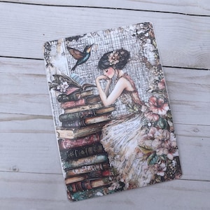 May include: A vintage-style illustration of a woman reading a book, surrounded by a stack of books, flowers, and a hummingbird. The background is a distressed, textured paper with a grid pattern.