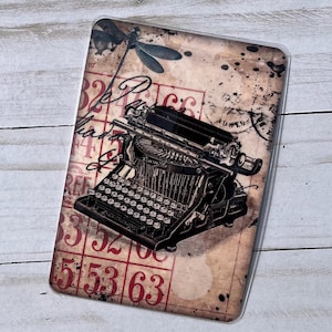 May include: Vintage typewriter with a dragonfly and numbers on a distressed background. The typewriter is black and has a silver carriage return lever. The background is a faded brown with red numbers and a dragonfly.