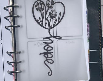 Puede incluir: Un separador de papel vegetal translúcido para agenda de anillas con una ilustración de línea negra de tres flores dentro de un corazón sobre la palabra hope escrita en letra cursiva, sujeto por anillas de metal plateado de la agenda.