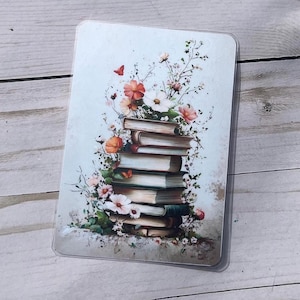 Puede incluir: Una tarjeta rectangular con una pila de libros adornada con flores y follaje. Los libros tienen páginas envejecidas y están rodeados de flores rosas, naranjas y blancas. Se ve una pequeña mariposa roja. El fondo es de un azul claro suave.