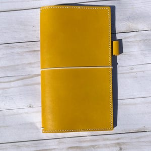 May include: A yellow leather bound journal with a white elastic closure and a yellow leather strap.
