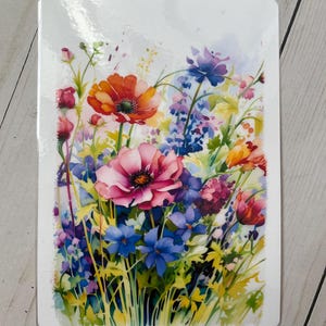 Pode incluir: Uma pintura em aquarela de um buquê de flores coloridas, incluindo flores rosa, vermelhas, laranja, azuis e roxas. As flores estão dispostas em um vaso e são cercadas por folhas verdes.