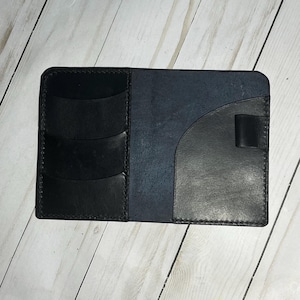 Puede incluir: Una cartera de cuero negro con múltiples ranuras para tarjetas y un cierre de solapa. La cartera tiene un interior de cuero azul.