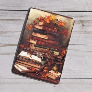 Puede incluir: Una pila de libros antiguos con cubiertas de cuero, adornada con hojas de otoño, se encuentra sobre una mesa de madera con una taza y otros objetos decorativos.