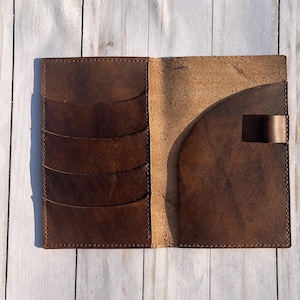 May include: Open brown leather wallet with multiple card slots and a large pocket. The wallet is made of distressed leather and has a simple, functional design. The interior is a lighter shade of brown.