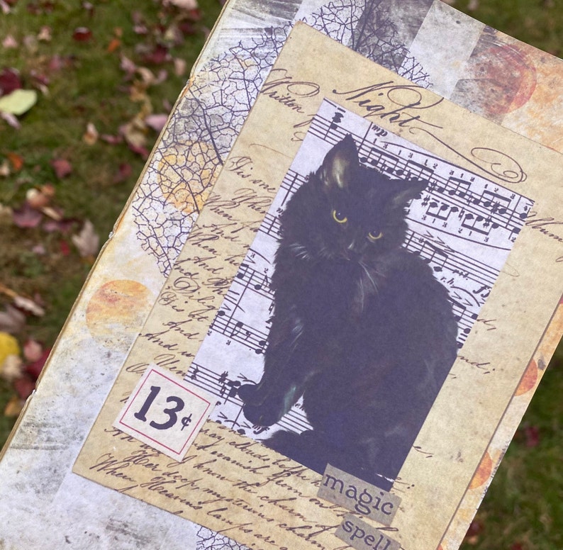 May include: A black cat with green eyes sits on a sheet of music with the word "Night" written in cursive. The music sheet is layered on top of a piece of paper with handwritten text and a price tag that says "13 cents". The image has a vintage aesthetic.