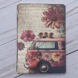 May include: A decorative case featuring a vintage-style illustration. The design includes a pink van adorned with floral patterns and a backdrop of aged paper with handwritten script. Large pink flowers are scattered across the design.