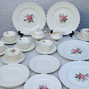 Puede incluir: Juego de té de porcelana blanca con diseño de rosas. El juego incluye tazas, platillos, platos, azucarero y jarrita para la leche. Los platos tienen un borde decorativo y texturizado.