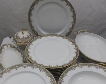 May include: A set of white porcelain dinnerware with a gold rim and floral pattern. The set includes a large platter, a soup bowl, a sugar bowl, and a stack of dinner plates.