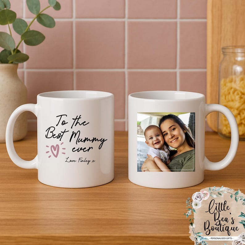 May include: White ceramic mug with a photo of a mother and child. The other mug has the text "To the Best Mummy ever" with a heart and the name "Finley".