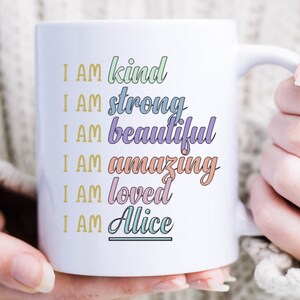 Op de afbeelding: Witte keramische mok met de tekst "I AM kind, I AM strong, I AM beautiful, I AM amazing, I AM loved, I AM Alice" in kleurrijke tekst.