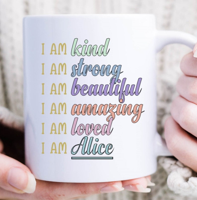 Op de afbeelding: Witte keramische mok met de tekst "I AM kind, I AM strong, I AM beautiful, I AM amazing, I AM loved, I AM Alice" in kleurrijke tekst.