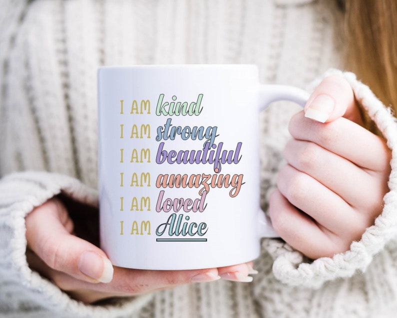 Op de afbeelding: Witte keramische mok met een kleurrijk ontwerp met de tekst "I AM kind, I AM strong, I AM beautiful, I AM amazing, I AM loved, I AM Alice".