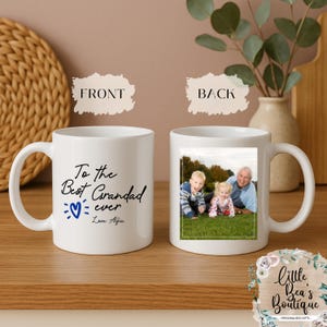 May include: White ceramic mug with a handle, featuring a photo on the back and text on the front that reads "To the Best Grandad ever Love Alfie" with a blue heart. The back of the mug has a photo of three people.
