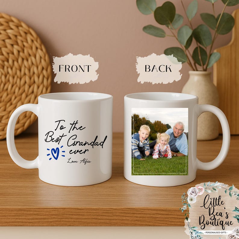 May include: White ceramic mug with a handle, featuring a photo on the back and text on the front that reads "To the Best Grandad ever Love Alfie" with a blue heart. The back of the mug has a photo of three people.
