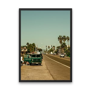 Könnte beinhalten: Ein grüner Vintage-Van, der auf einer Straße mit Palmen am Straßenrand geparkt ist. Der Van hat ein Surfbrett auf dem Dach und eine Person sitzt auf dem Beifahrersitz. Die Straße ist leer, bis auf ein paar Autos in der Ferne.