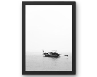 May include: A black and white photograph of a longtail boat in the ocean. The boat is anchored in the water with a person sitting in the back. The sky is cloudy and the water is calm.