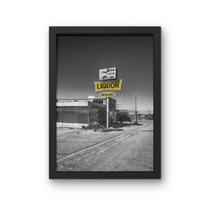 Könnte beinhalten: Ein Schwarzweißfoto eines verlassenen Spirituosenladens mit einem Schild, auf dem "El Loco Liquors Grocery" steht. Das Schild ist gelb mit schwarzen Buchstaben. Der Laden befindet sich in einer Wüstenregion mit einer unbefestigten Straße, die zu ihm führt.