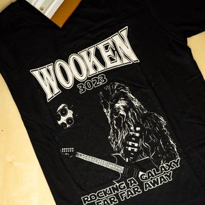 Może przedstawiać: Czarny T-shirt z białym nadrukiem Chewbaccy grającego na gitarze z tekstem "Wooken 3023 Rocking a Galaxy Far Far Away"