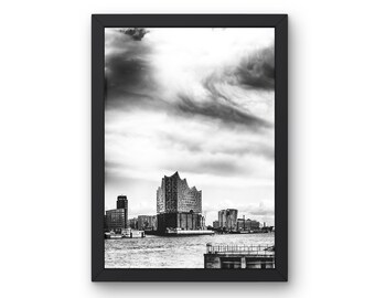 Puede incluir: Fotografía en blanco y negro de un horizonte urbano con un gran edificio en el centro. El edificio tiene un diseño único y angular y está rodeado de otros edificios y agua. El cielo está nublado y dramático.