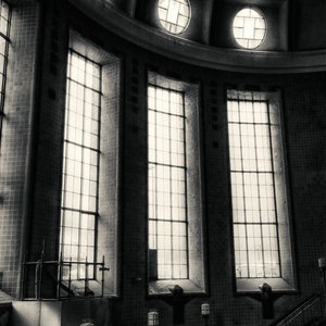 May include: Black and white photo of a building interior with a vaulted ceiling and large windows. The windows are divided into panes of glass. The building has a tiled floor and a staircase.