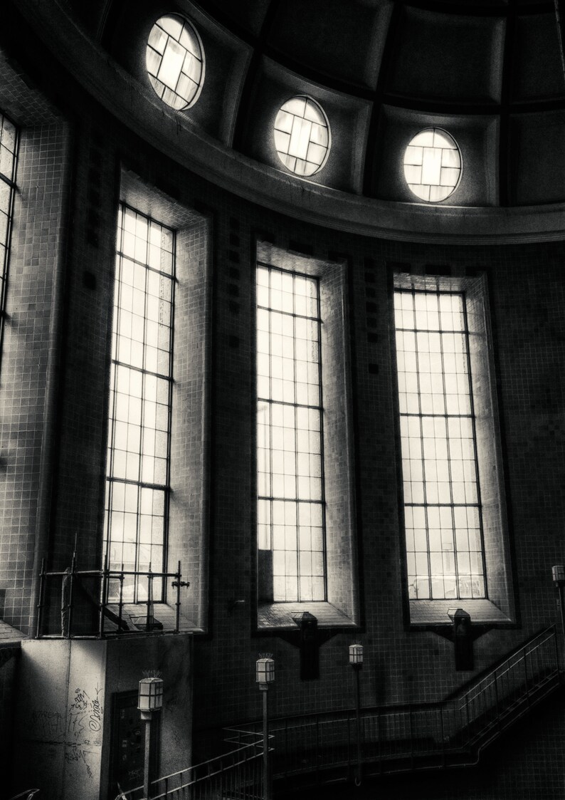 May include: Black and white photo of a building interior with a vaulted ceiling and large windows. The windows are divided into panes of glass. The building has a tiled floor and a staircase.