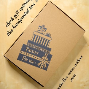May include: A brown cardboard box with a hand-printed design of a stack of presents. The design includes the words "Present" and "For You!" The box is on a light wood surface. The text "Regular Box comes without print" is visible on the bottom right corner of the box.