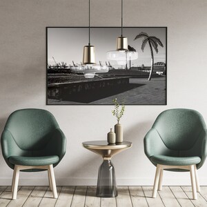 May include: Two green chairs with wooden legs and a glass and gold side table in front of a black and white photograph of a palm tree and a cityscape.